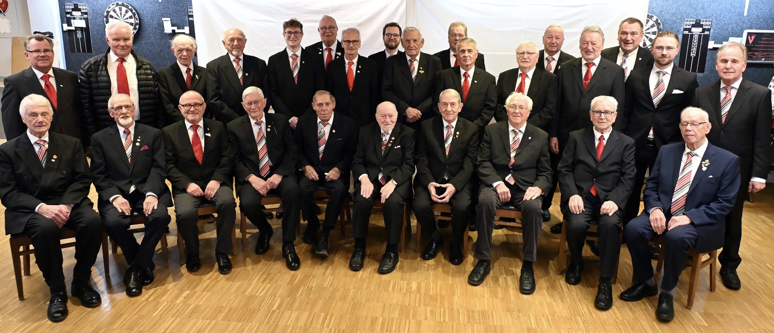 Gruppenfoto der Chorgemeinschaft Q.V. Rheingold-Münster u. MGV Rinkerode in Vereinskleidung: Anzüge mit Vereinskrawatte und Vereinsnadel, aufgenommen im Probenraum unserer Vereinskneipe Mauritius