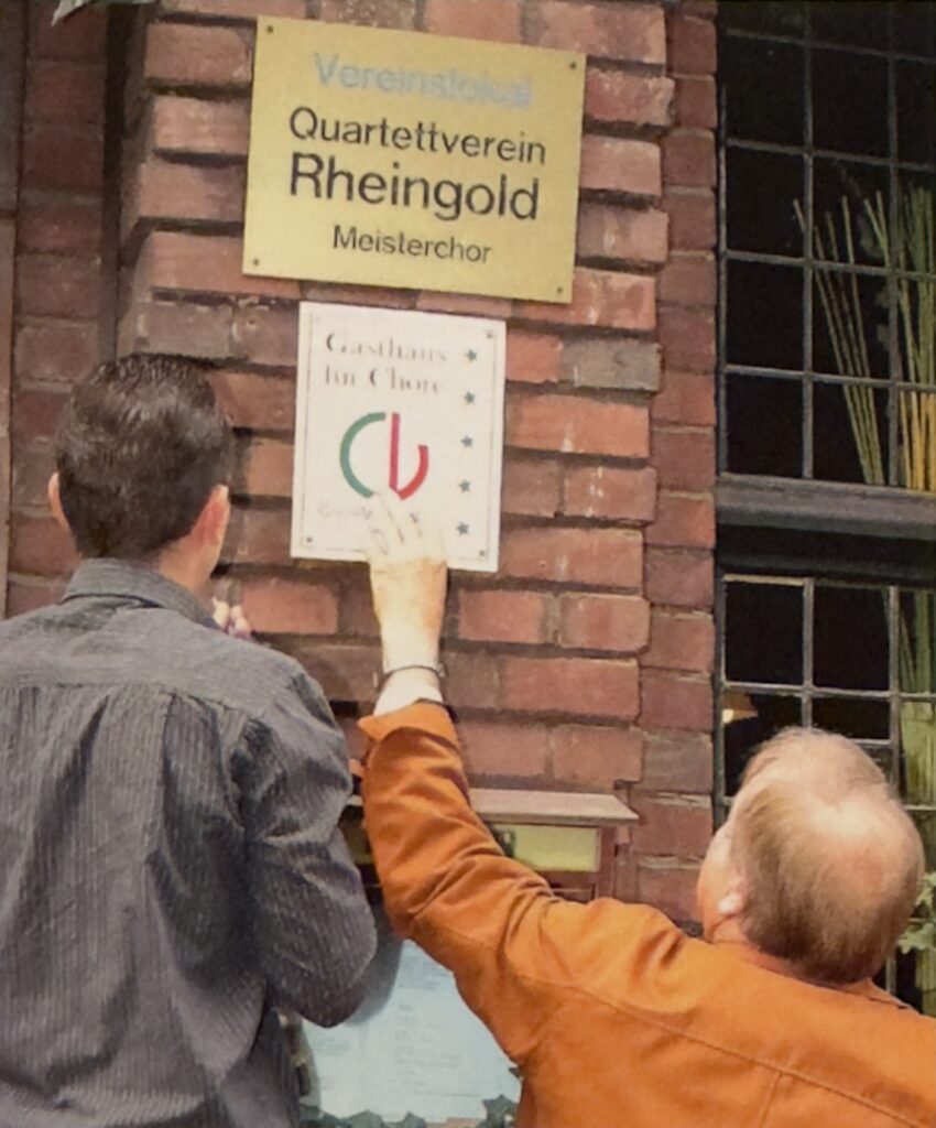 An der Fassade des Hubertihofs wird die Plakette &sbquo;Gasthaus f&uuml;r Ch&ouml;re&lsquo; unterhalb der bereits vorhandenen Plakette &sbquo;Vereinslokal Quartettverein Rheingold Meisterchor&lsquo; angebracht.